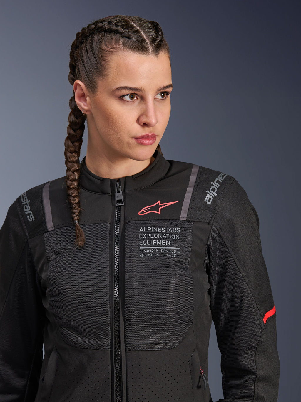 Casaco Alpinestars Stella ST-2 Air, casaco de motociclismo para mulher em preto, com painéis de malha para fluxo de ar, marca "Alpinestars Exploration Equipment" com coordenadas e logótipo vermelho no peito, usado por uma modelo com cabelo entrançado.