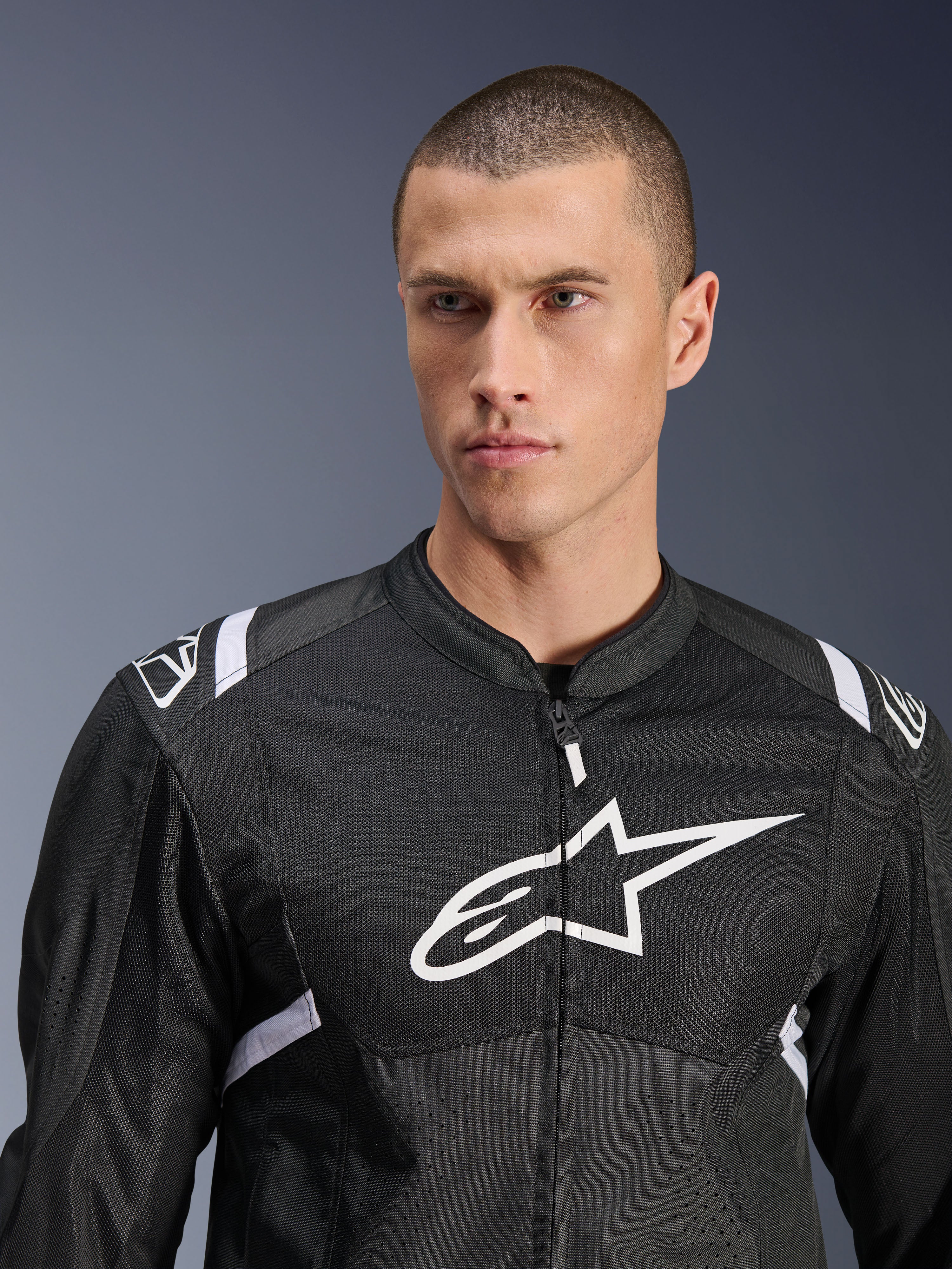 Casaco Alpinestars T-SPS Air V2, casaco de motociclismo têxtil, preto e branco, com grande logótipo branco no peito e painéis em malha, corte desportivo de performance usado por modelo masculino