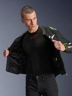Male model wearing the Alpinestars T-Sps Air V2 Jacket in Black and Yellow Fluo, shown open to highlight the internal mesh construction and pocketing, paired with a black Alpinestars base layer and black pants, urban motorcycle riding gear style