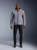 Model wearing Alpinestars Chrome V2 Sport Hoodie in Gray Heather Red Fluo, light gray tech fleece hoodie with a bright orange-red star logo on the chest, paired with black pants and dark sneakers, casual urban motorcycle riding style