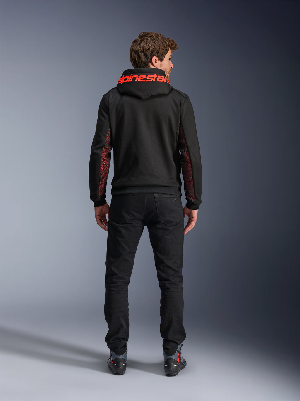 Alpinestars Chrome Air Sport Hoodie, preto e vermelho flúor, vista de costas de um homem a usar casaco de motociclismo casual, com a marca Alpinestars a vermelho no capuz e painéis de malha vermelha nas mangas, combinado com calças pretas.