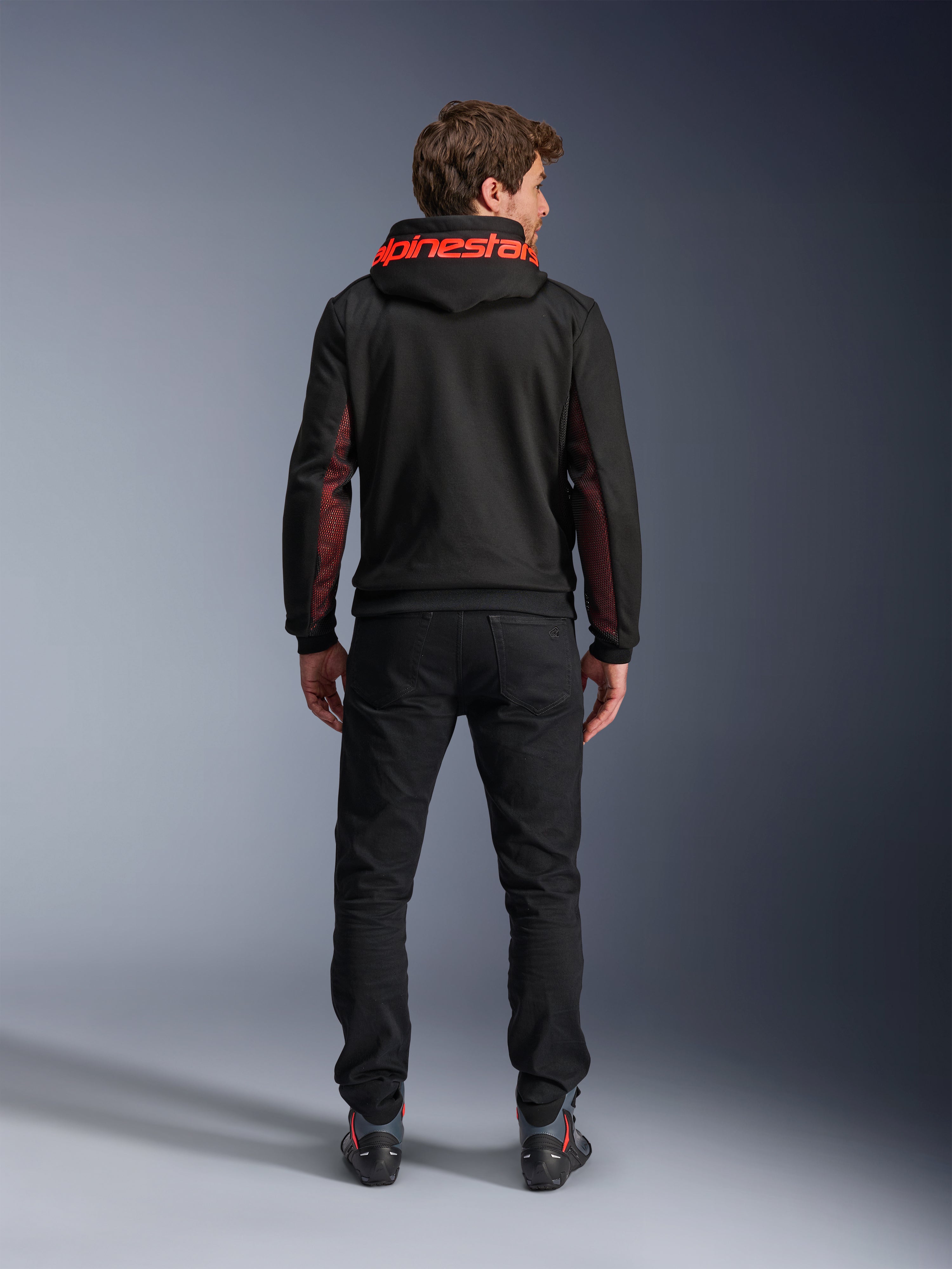 Alpinestars Chrome Air Sport Hoodie, preto e vermelho flúor, vista de costas de um homem a usar casaco de motociclismo casual, com a marca Alpinestars a vermelho no capuz e painéis de malha vermelha nas mangas, combinado com calças pretas.