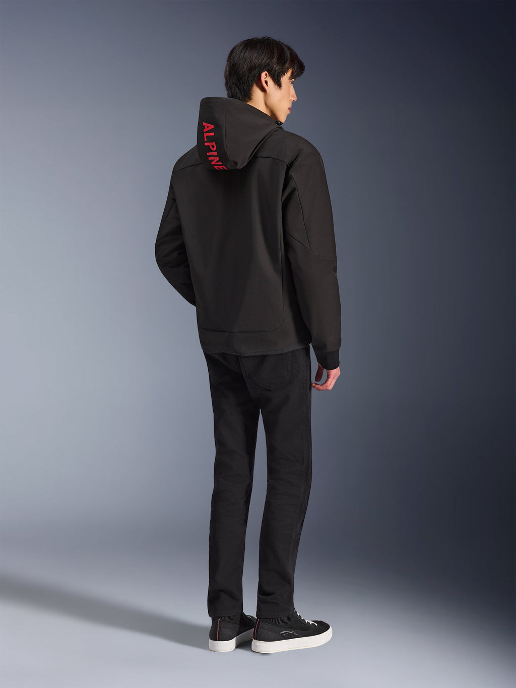 Alpinestars Radium Tech Hoodie, Black with red Alpinestars branding on the hood, back view on a male model, worn with black pants and sneakers, technical urban riding gear