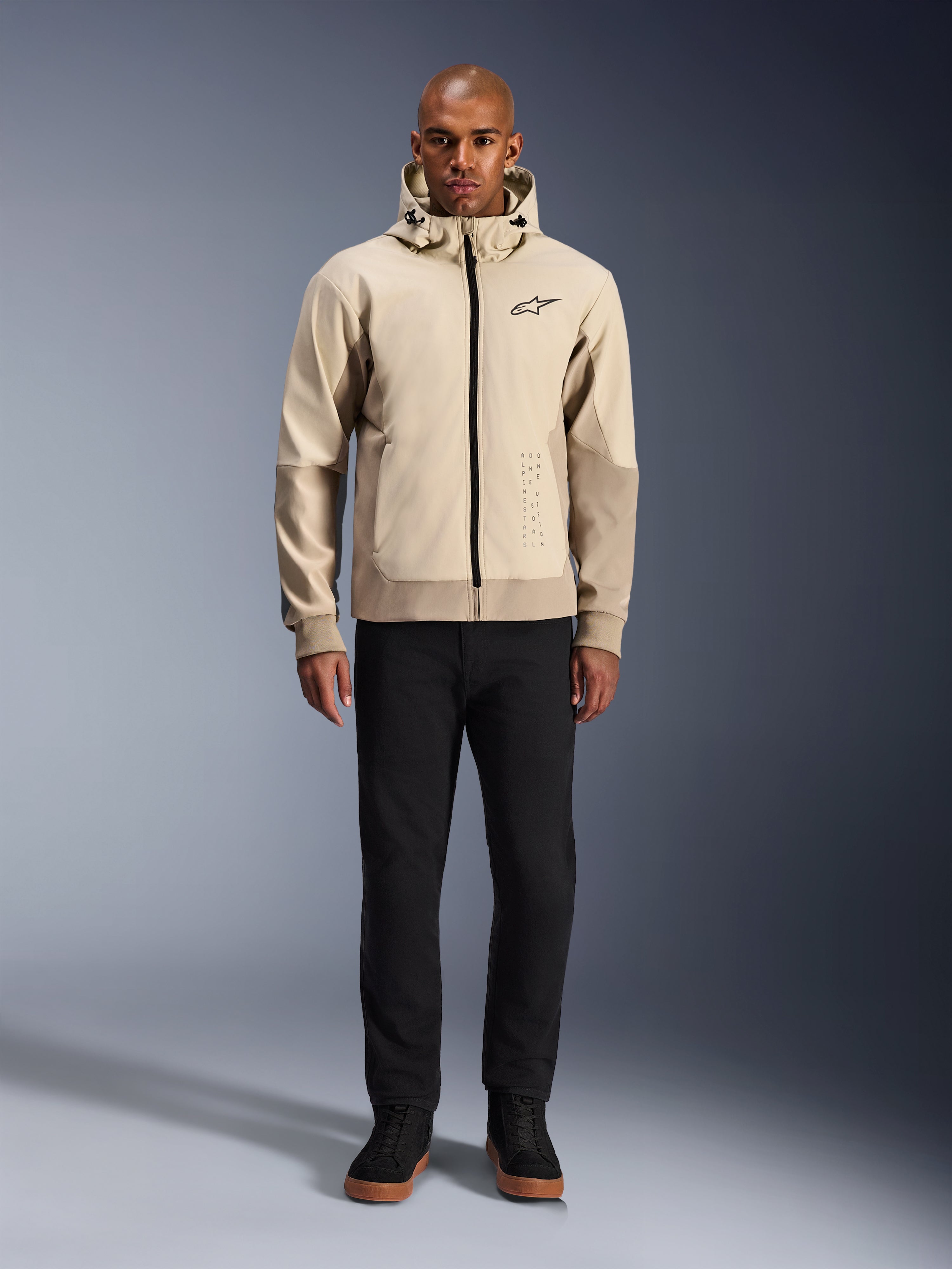 Alpinestars Radium Tech Hoodie in Mastic Aluminum, urban motorcycle hoodie worn by a male model with black pants and black boots, featuring a full-length black zipper, small chest logo, and athletic fit for city riding.