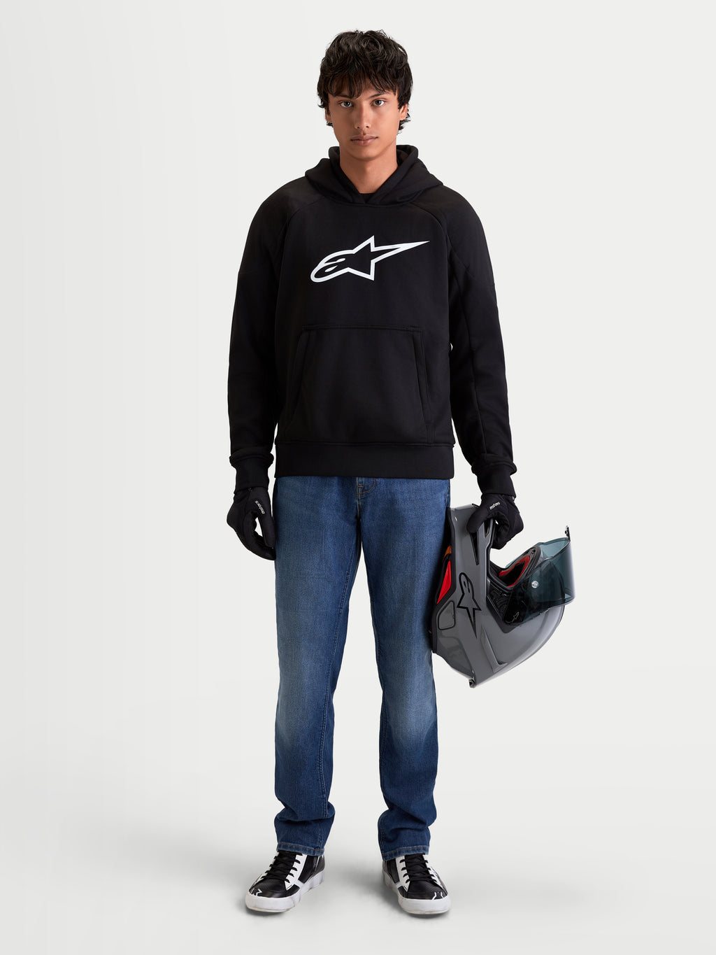 Alpinestars Ageless Hoodie, casaco de moto urbano para homem, preto e branco com logótipo Astar no peito, num modelo a segurar um capacete e a usar luvas de moto, vestuário de proteção casual certificado CE