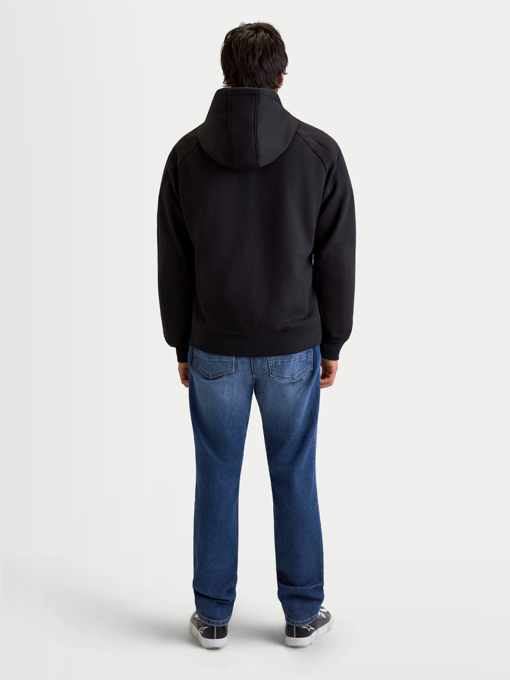 Alpinestars Ageless Hoodie, casaco de moto urbano para homem em preto, vista traseira num modelo a usar calças de ganga e sapatos de moto casual, com capuz fixo e construção têxtil protetora