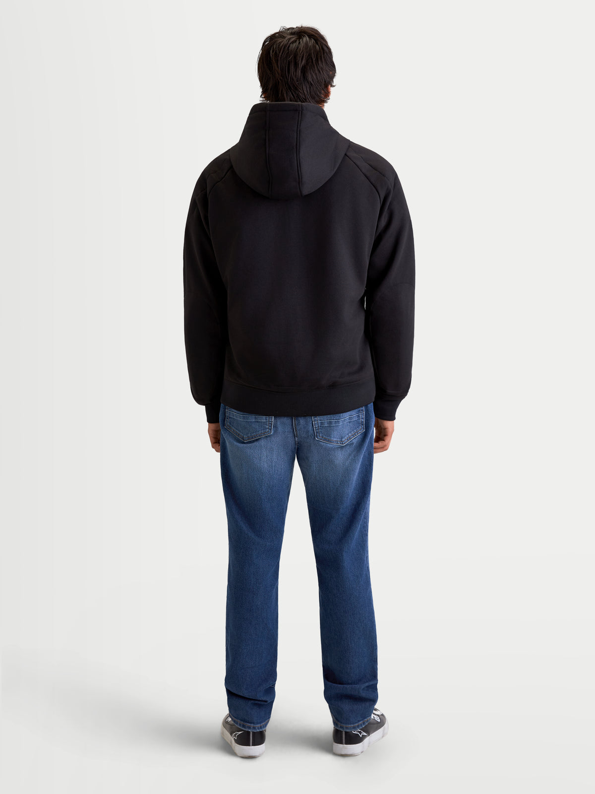 Alpinestars Ageless Hoodie, casaco de moto urbano para homem em preto, vista traseira num modelo a usar calças de ganga e sapatos de moto casual, com capuz fixo e construção têxtil protetora