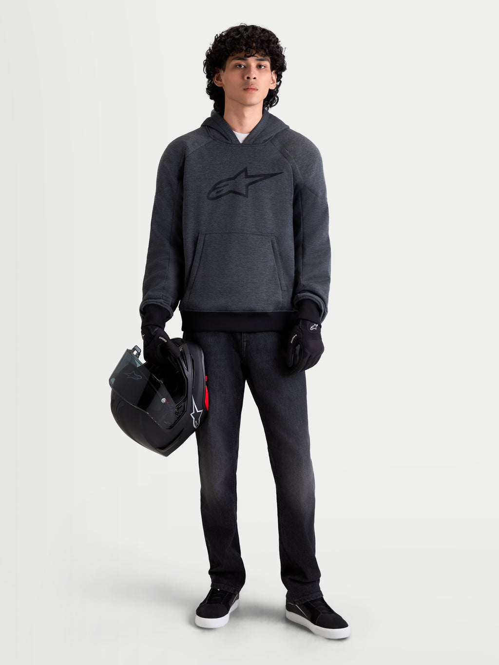 Alpinestars Ageless Hoodie, blusão de moto urbano para homem em cinzento melange de asfalto, vista frontal num modelo a usar luvas de moto pretas e a segurar um capacete, com proteção integrada nos ombros e cotovelos