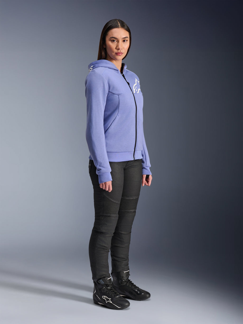 Alpinestars Hoodie Feminino Stella Chrome V2 Sport, hoodie de motociclismo em azul-violeta com logótipo Alpinestars branco no peito, vestido por uma modelo com calças de condução pretas e botas de motociclismo pretas, vestuário de condução urbana para mulher