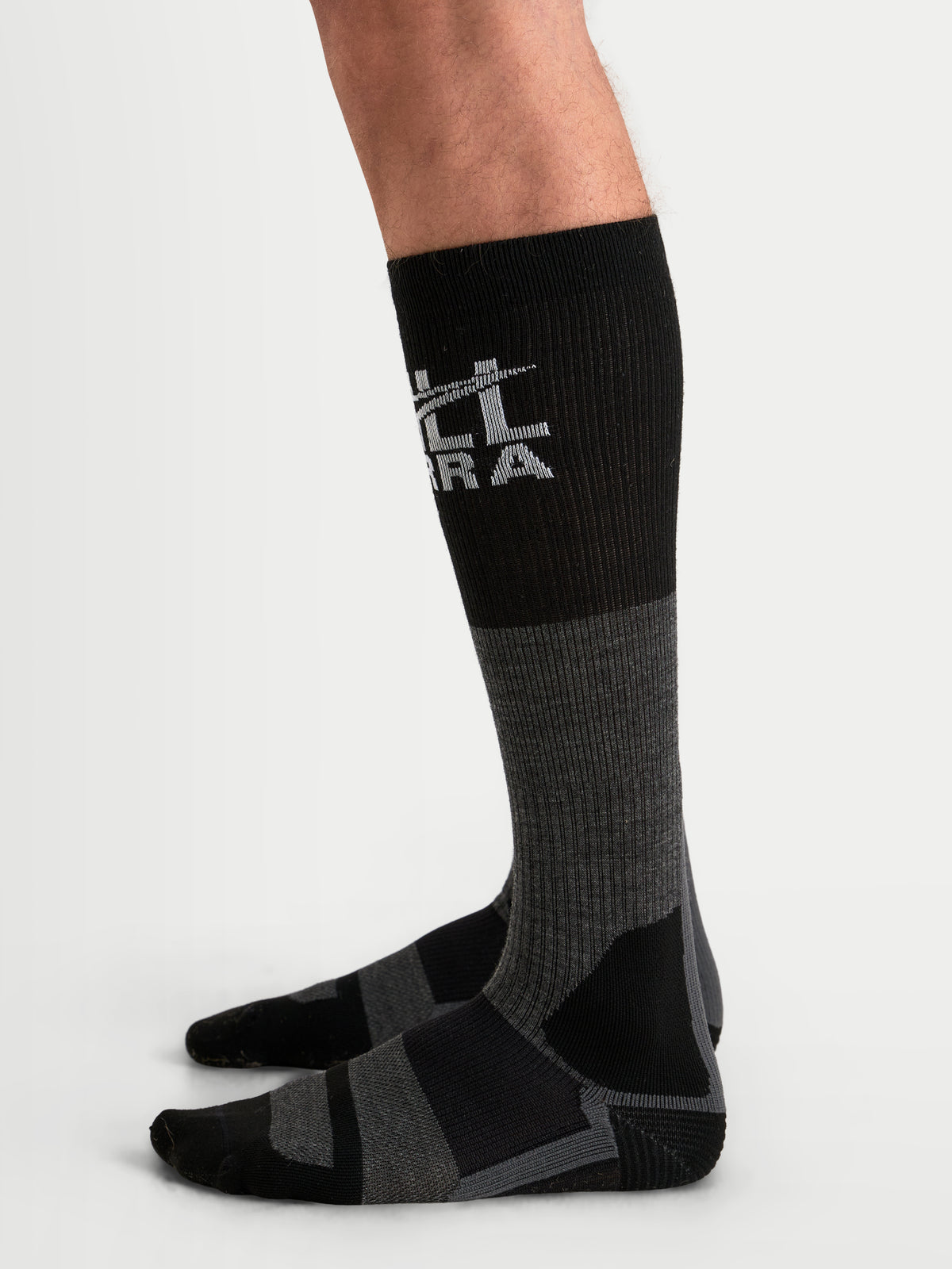 Alpinestars AT-8 Merino Socks, over-the-calf adventure motorcycle socks, tar gray and black, merino wool thermal blend with ribbed upper calf and reinforced heel and toe, worn on a model