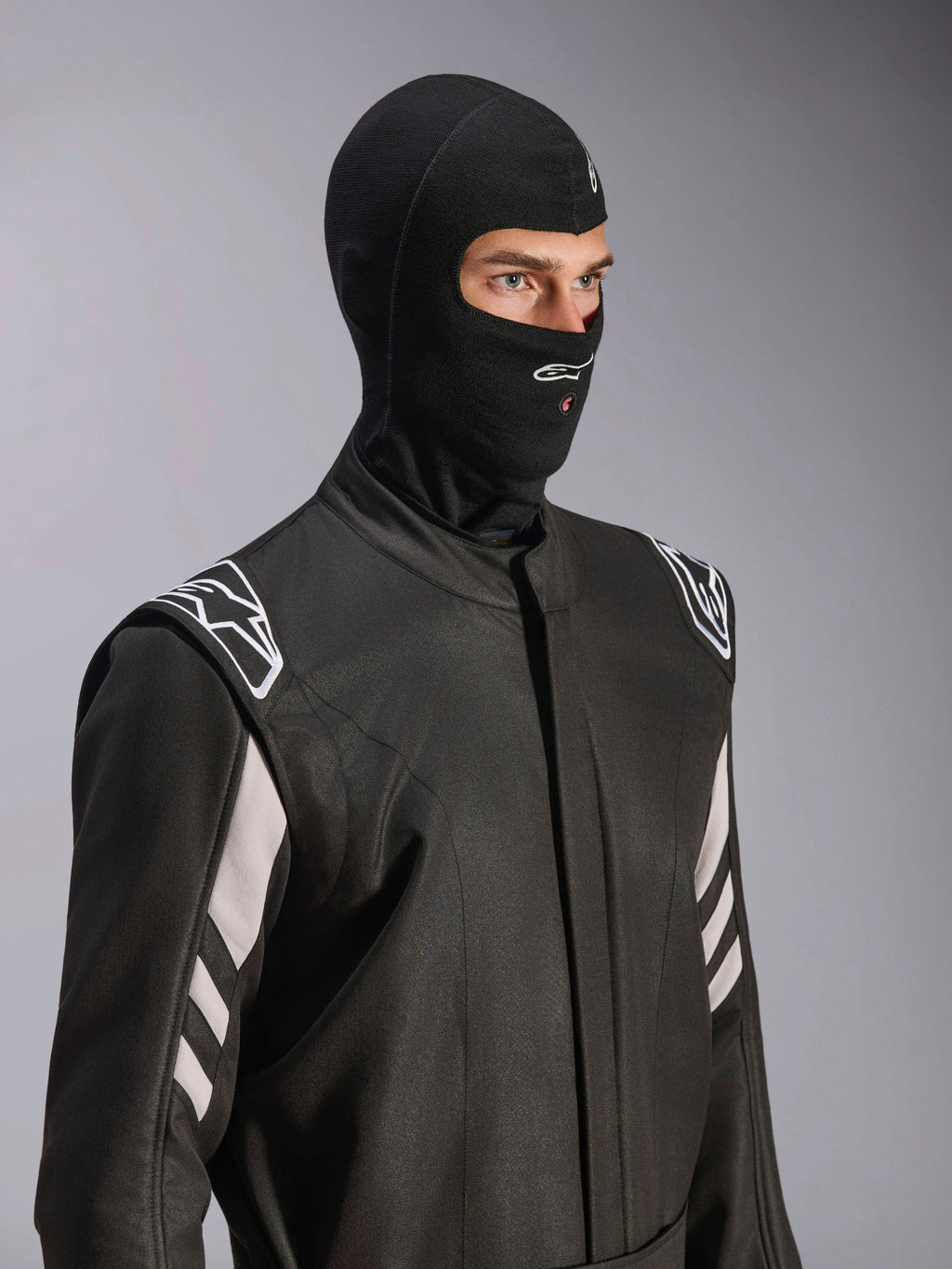 Alpinestars ZX Evo V3 Balaclava, preta, balaclava resistente ao fogo para automobilismo, usada por um modelo num fato de corrida preto com detalhes brancos, apresenta o logótipo Alpinestars no queixo, abertura para tubo de hidratação, equipamento de proteção profissional para desportos motorizados