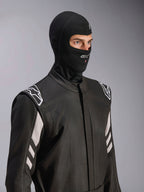 Alpinestars ZX Evo V3 Balaclava, preta, balaclava resistente ao fogo para automobilismo, usada por um modelo num fato de corrida preto com detalhes brancos, apresenta o logótipo Alpinestars no queixo, abertura para tubo de hidratação, equipamento de proteção profissional para desportos motorizados