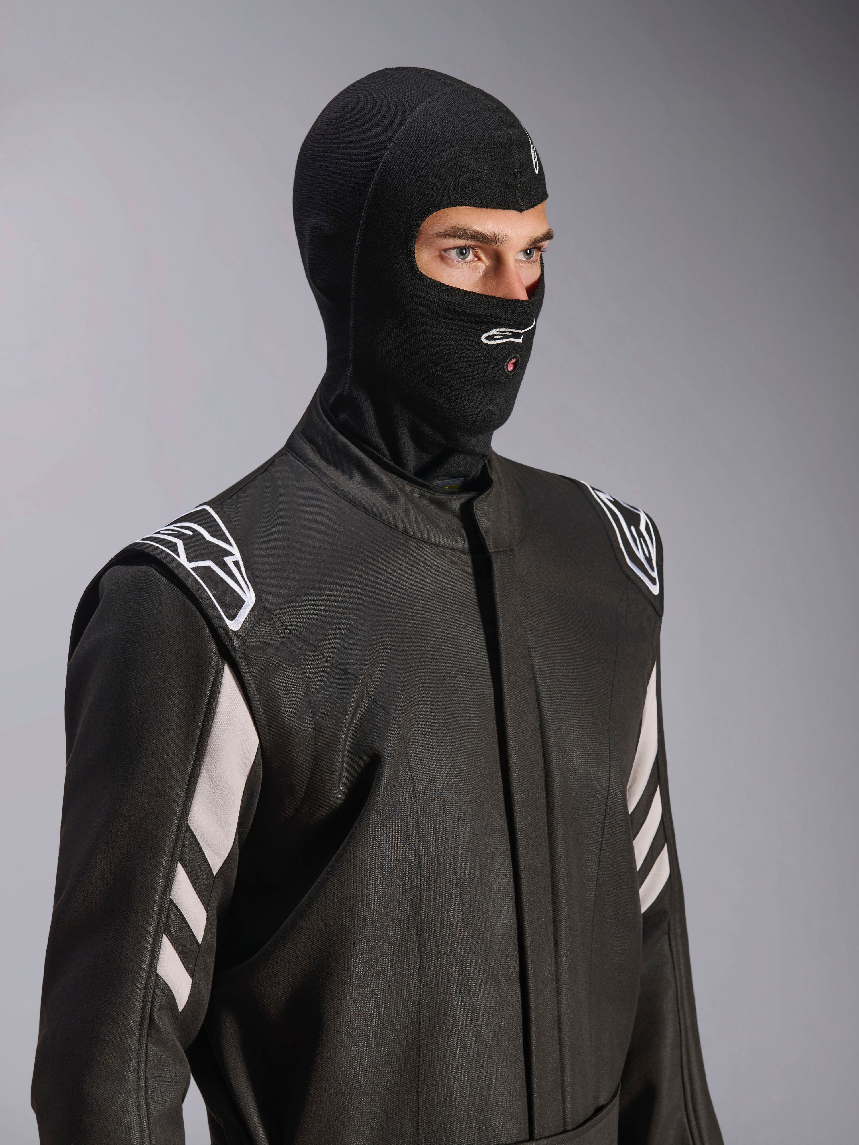 Alpinestars ZX Evo V3 Balaclava, preta, balaclava resistente ao fogo para automobilismo, usada por um modelo num fato de corrida preto com detalhes brancos, apresenta o logótipo Alpinestars no queixo, abertura para tubo de hidratação, equipamento de proteção profissional para desportos motorizados