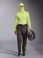 Balaclava Alpinestars ZX Evo V3 em amarelo fluo, usada com camisola de camada de base de manga comprida a condizer e calças de automobilismo cinzento escuro, modelo masculino a segurar um capacete de fibra de carbono, equipamento profissional de automobilismo