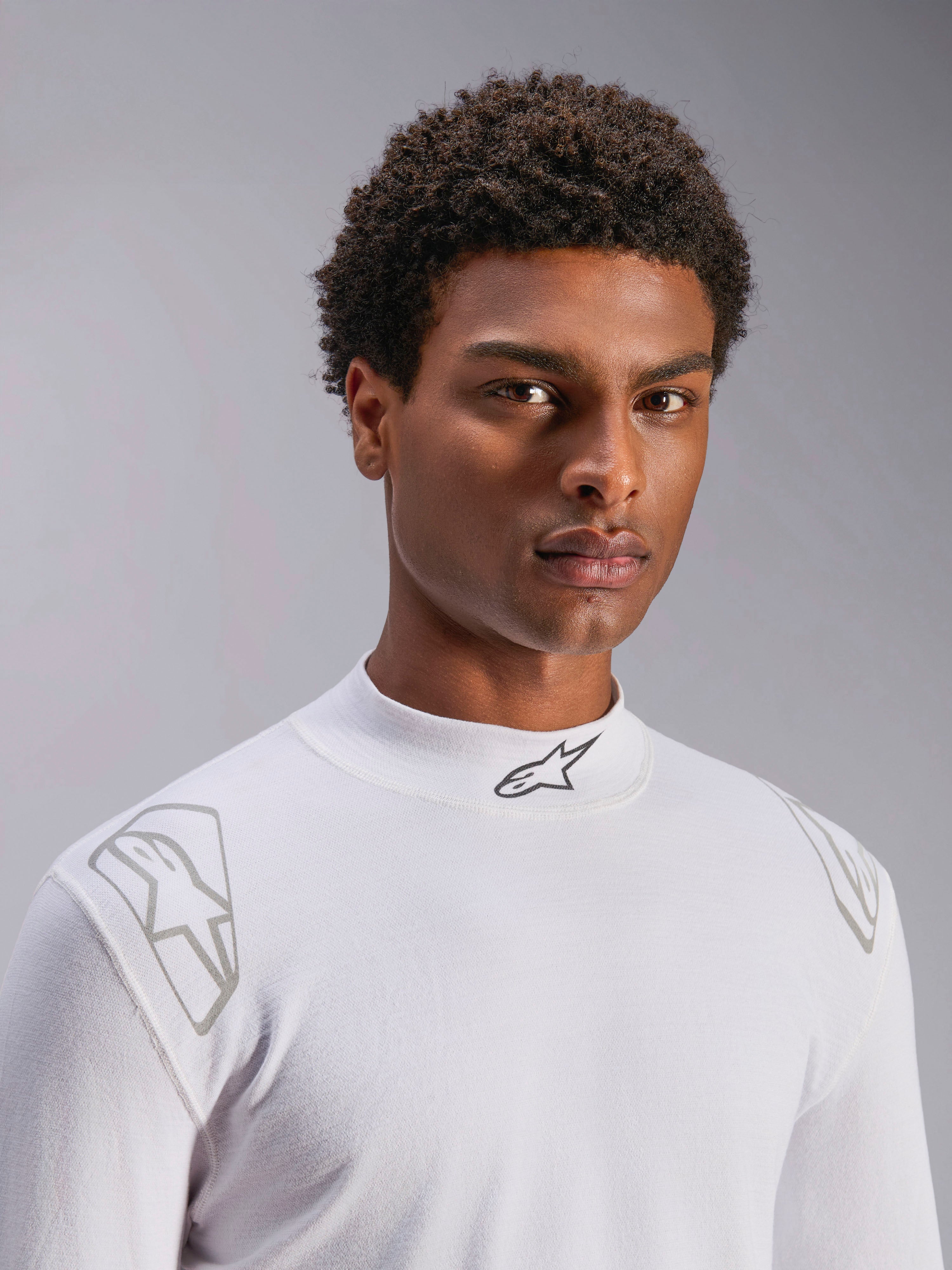 Alpinestars ZX Evo V3 Top - Manga Comprida, camada de base branca para automobilismo, vestido por um modelo masculino, gola subida com logótipo Alpinestars preto, grafismos prateados nos ombros, roupa interior de desporto motorizado leve e resistente a chamas