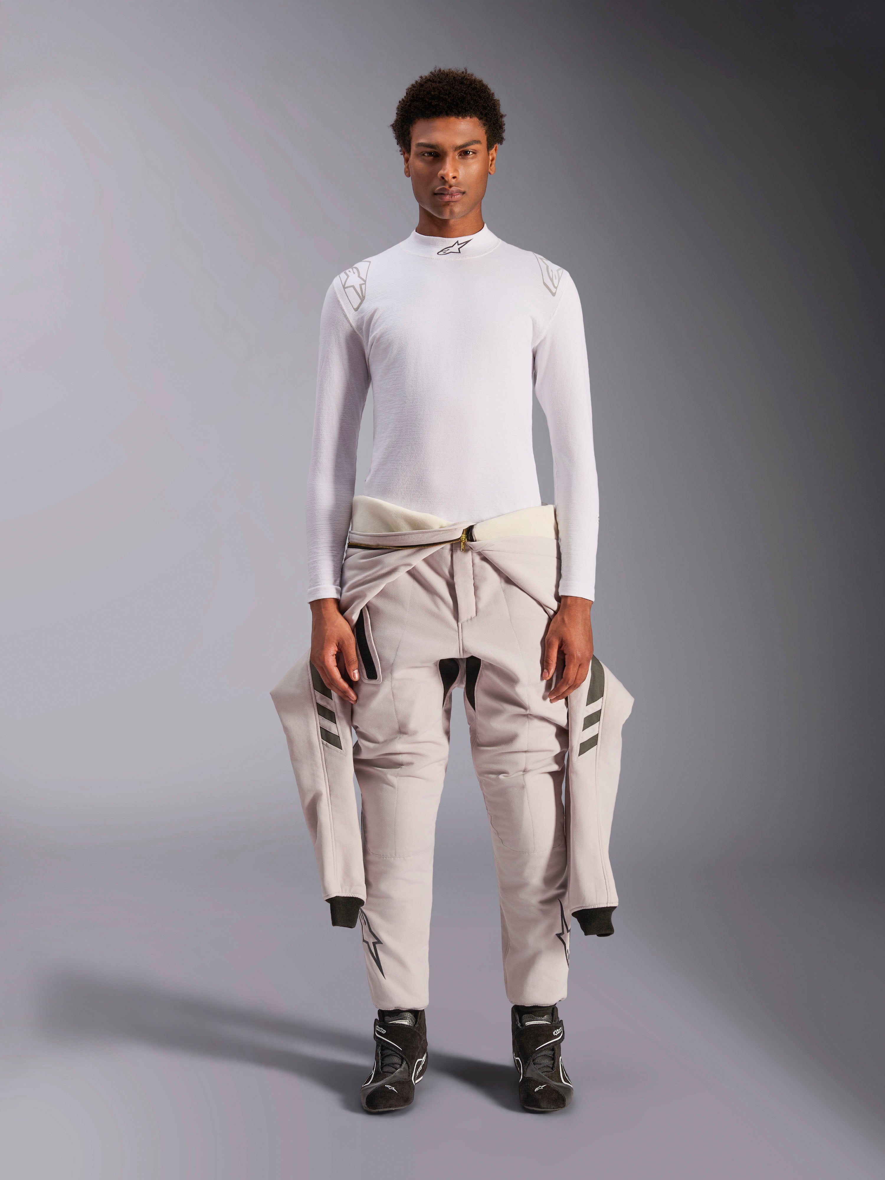 Alpinestars ZX Evo V3 Top, Manga Comprida, Branco, camada base para automobilismo usada com um fato de competição de cor clara atado à cintura e botas de competição pretas, com gola alta com logótipo e marca nos ombros, roupa interior de desporto motorizado profissional resistente a chamas