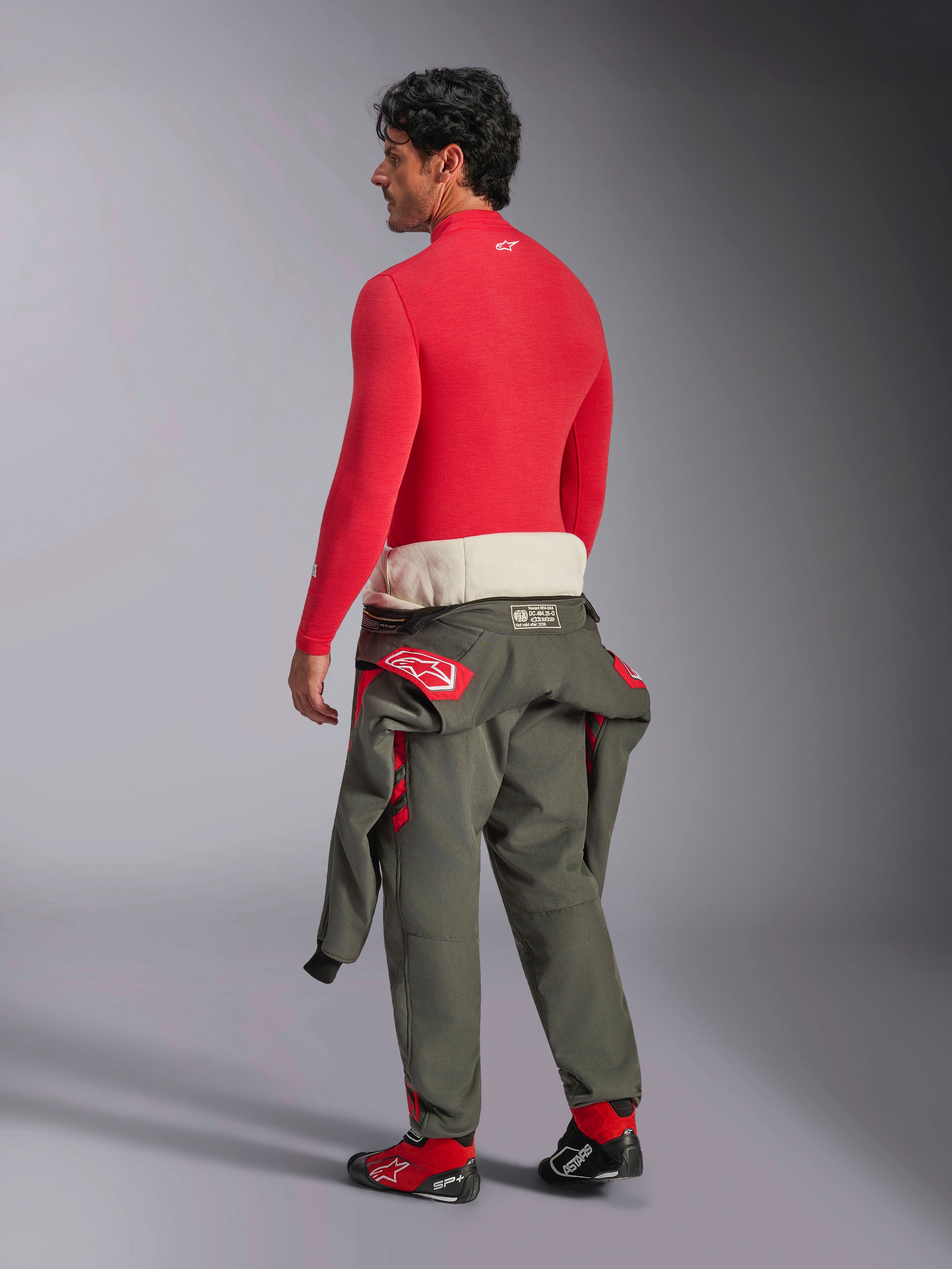 Alpinestars ZX Evo V3 Long Sleeve Top, camada de base para automobilismo em vermelho, vista traseira de um modelo masculino a usar calças de fato de corrida verde azeitona à cintura e botas de corrida vermelhas, roupa interior de performance resistente às chamas para desporto automóvel