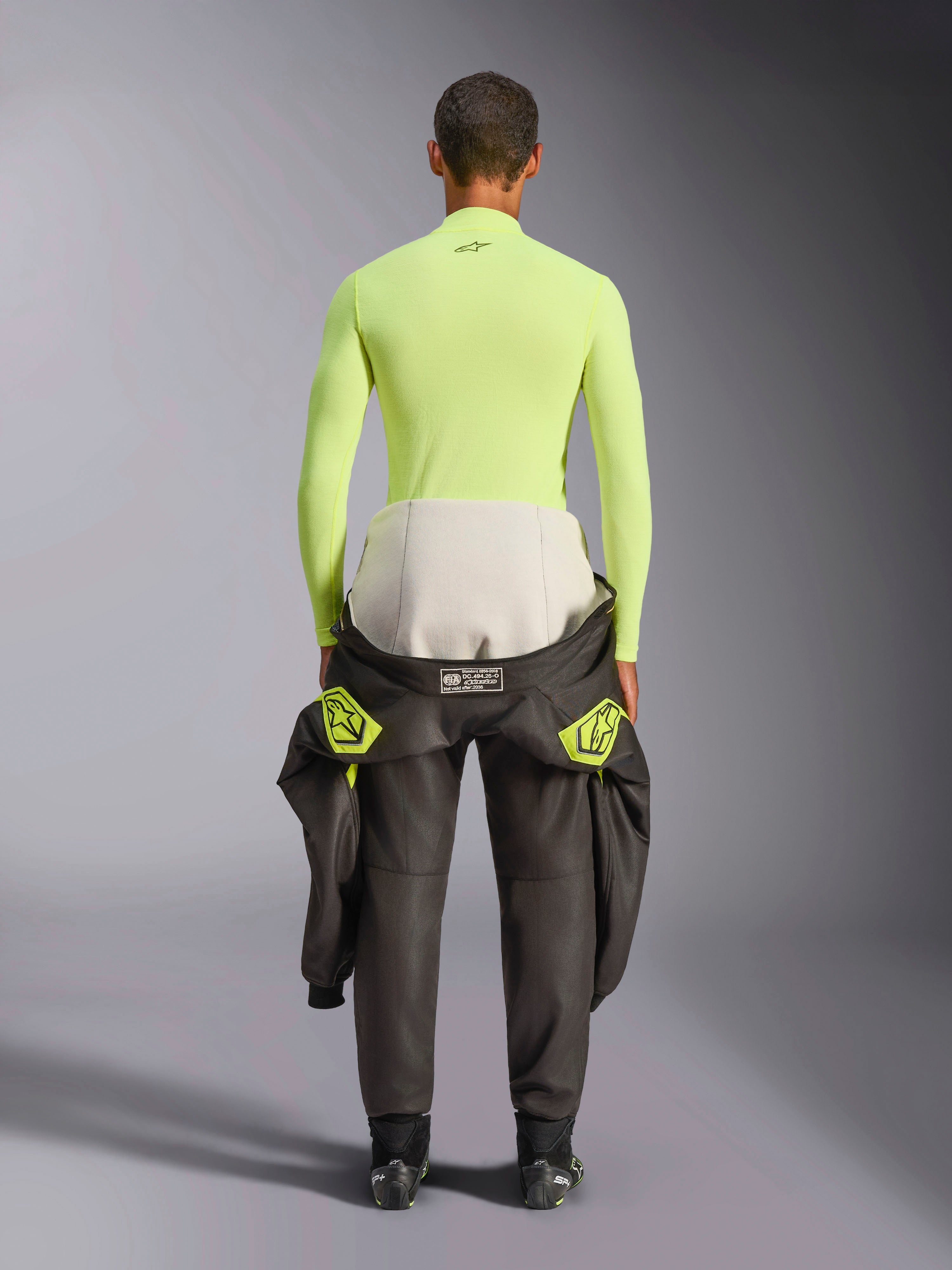 Alpinestars ZX Evo V3 Top, Camada de Base de Manga Comprida, Amarelo Fluo, vista traseira de um piloto com um fato de condução atado à cintura, top amarelo néon vibrante resistente às chamas com um pequeno logótipo preto na gola e um ajuste atlético justo