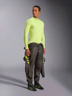 Alpinestars ZX Evo V3 Top - Manga Comprida, Amarelo Fluo, vestido por um modelo com um fato de competição cinzento escuro atado à cintura e botas de competição pretas, camada de base de automobilismo resistente às chamas, construção leve em malha jacquard, equipamento profissional de automobilismo