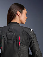 Mulher a usar Casaco de Couro Alpinestars Stella Dusk, couro preto com detalhes Diva Pink e logótipo branco no ombro, vista traseira a mostrar a marca DUSK e painéis elásticos em acordeão, design ergonómico desportivo