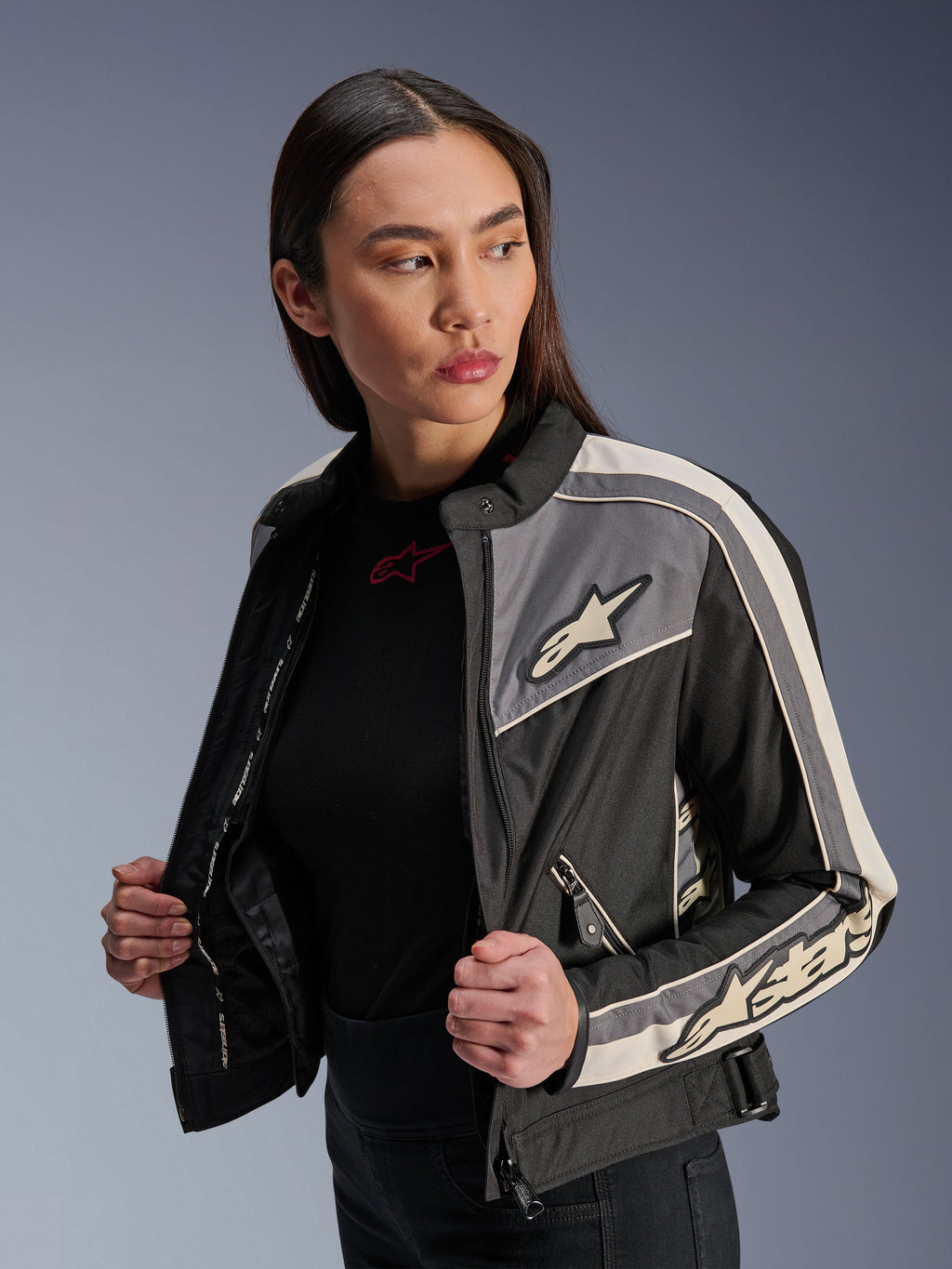 Casaco Alpinestars Stella T-Dyno WR para mulher, casaco de motociclismo têxtil, preto, cinzento escuro e cru, design de inspiração vintage com riscas desportivas e logótipos no peito e mangas, vestido por uma modelo, equipamento de condução urbana