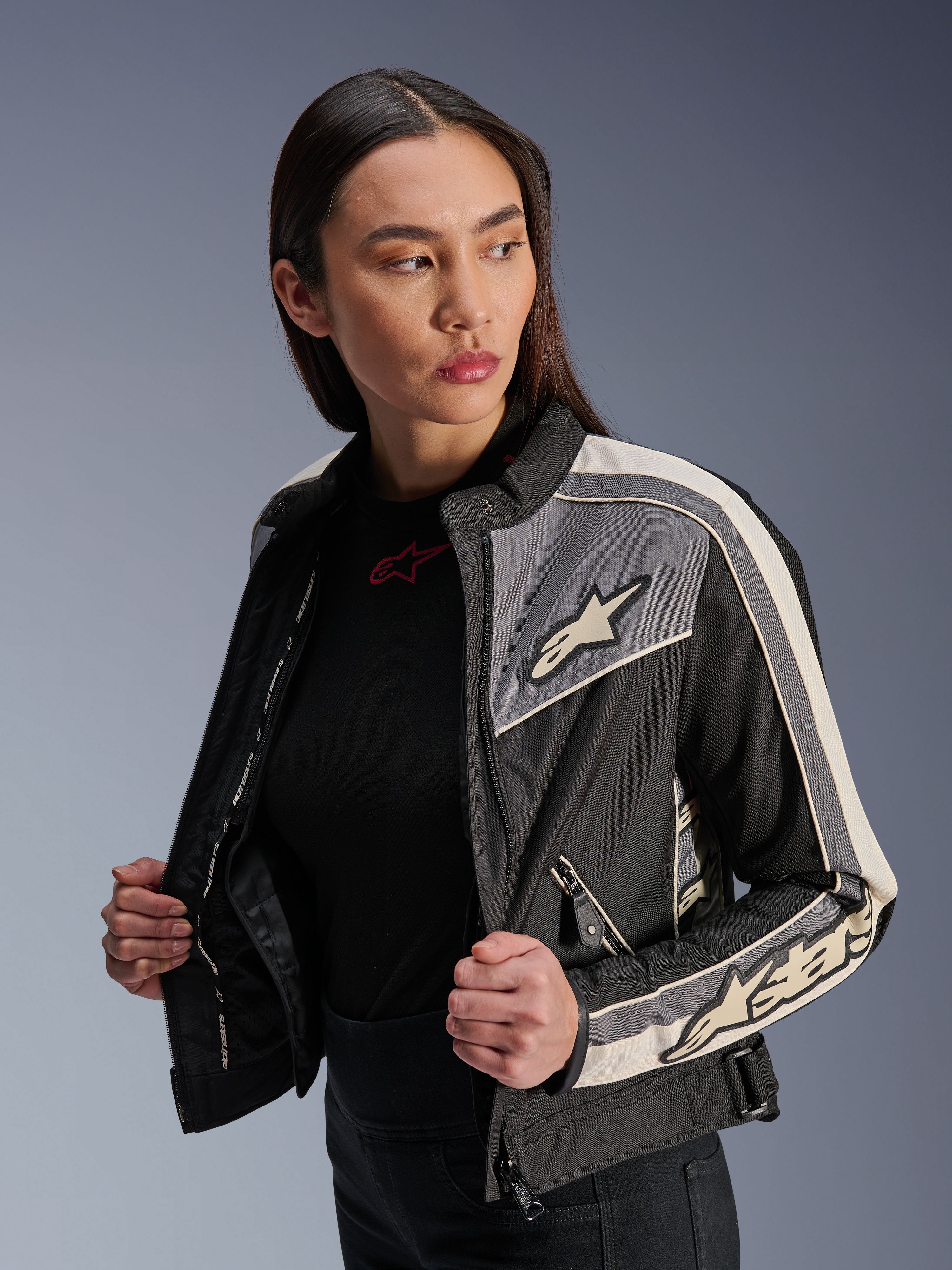 Casaco Alpinestars Stella T-Dyno WR para mulher, casaco de motociclismo têxtil, preto, cinzento escuro e cru, design de inspiração vintage com riscas desportivas e logótipos no peito e mangas, vestido por uma modelo, equipamento de condução urbana