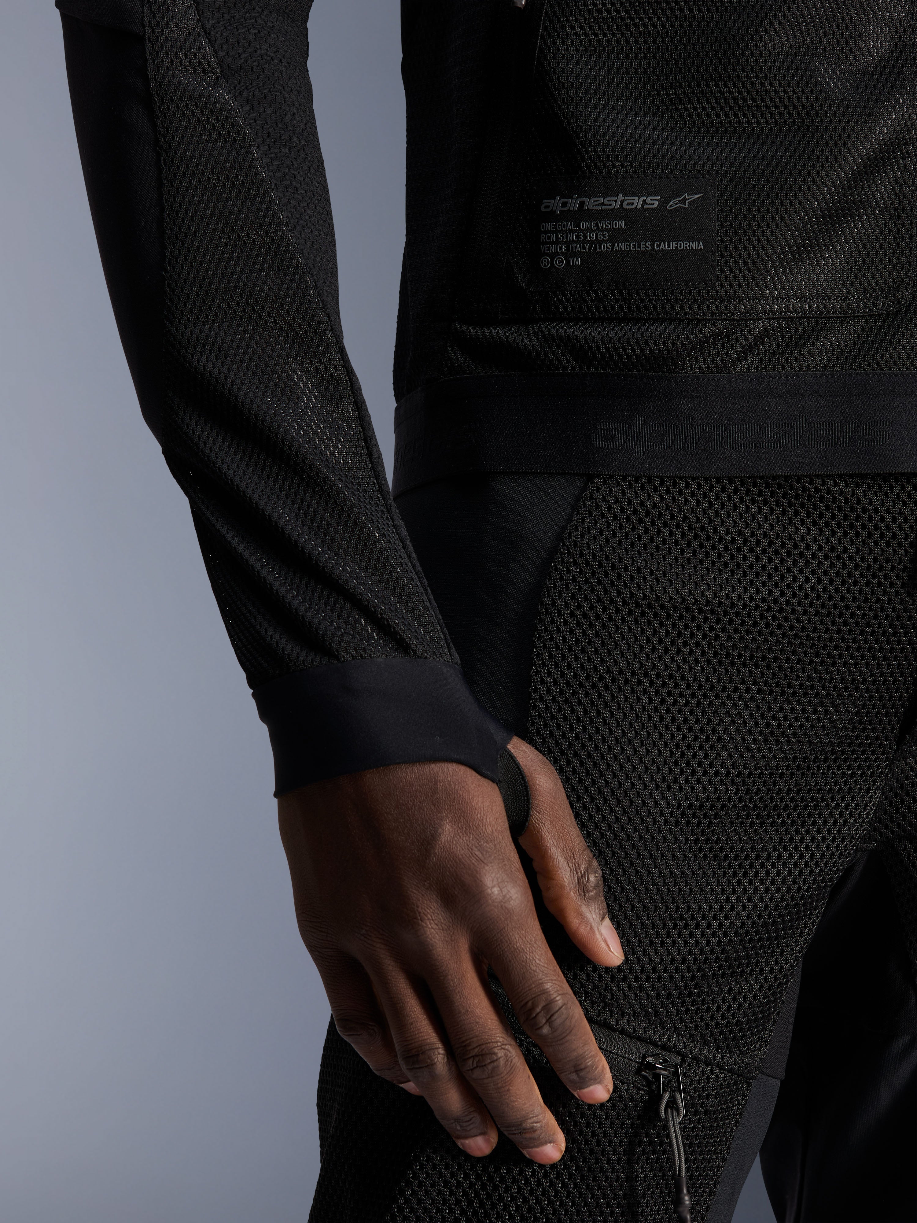 Alpinestars Troop-Air Jacket, preto, grande plano que mostra a construção em malha técnica, emblema da marca com texto técnico e manga com abertura integrada para o polegar, casaco de motociclismo urbano de verão com design de elevado fluxo de ar