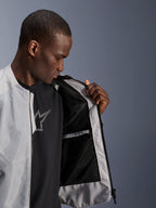 Modelo masculino a usar o Casaco Alpinestars C-1 Air em prateado, abrindo a frente para revelar o forro interior em malha técnica preta e um bolso interior impermeável com fecho de correr.