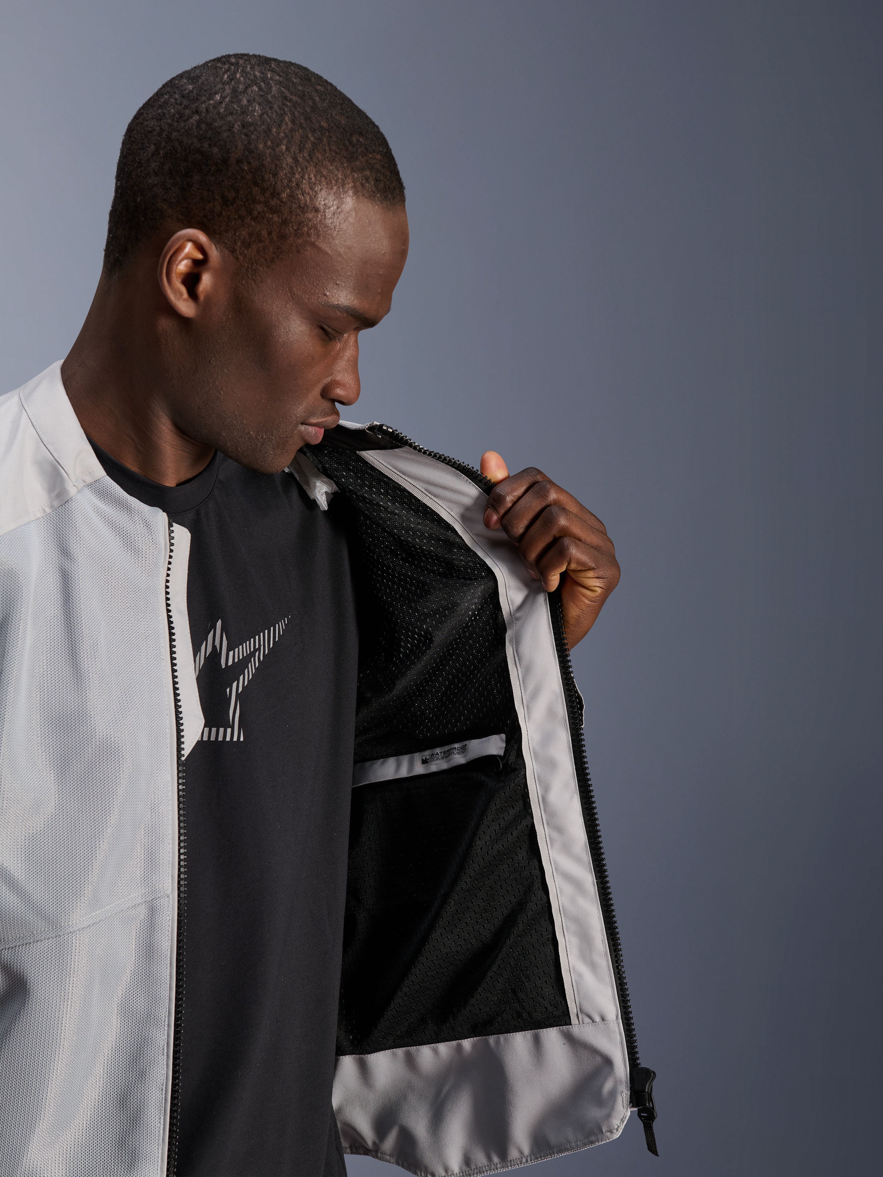 Modelo masculino a usar o Casaco Alpinestars C-1 Air em prateado, abrindo a frente para revelar o forro interior em malha técnica preta e um bolso interior impermeável com fecho de correr.