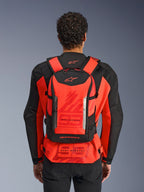 Mochila Alpinestars MM93 AMP3, mochila técnica de motociclismo, vermelho fluorescente e preto, vista de trás num condutor que usa um casaco de corrida MM93 vermelho e preto, com logótipos Alpinestars e branding Marc Márquez.