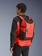 Mochila Alpinestars MM93 AMP3, mochila técnica de motociclismo, vermelho fluo e preto, usada por um modelo de costas sobre um casaco vermelho e preto a condizer, com gráficos '93' de Marc Marquez, alças ajustáveis e design desportivo e elegante