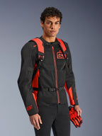 Mochila Alpinestars MM93 AMP3, vermelho fluo e preto, usada por um modelo com casaco e luvas de motociclismo MM93 a condizer em preto e vermelho, vista frontal destacando as alças ajustáveis e a fivela no peito, equipamento técnico inspirado em competição