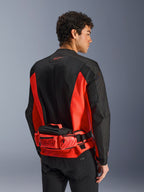 Alpinestars MM93 Waist Bag, bolsa de cintura para motociclismo, vermelho vivo e preto, usada sobre um casaco de motociclismo a condizer em preto e vermelho, com compartimentos com fecho de correr e logótipo MM93 de Marc Márquez, construção em têxtil resistente para motociclismo