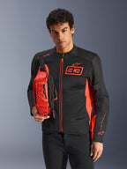 Homem a usar a Alpinestars MM93 Waist Bag, em vermelho fluo e preto, usada como mala tiracolo sobre um blusão de motociclismo preto e vermelho a condizer, com o logótipo Marc Marquez 93 e design desportivo de competição