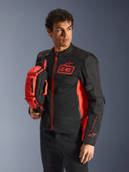 Alpinestars MM93 Waist Bag, bolsa de cintura em Vermelho Fluo e Preto, segurada por um modelo a usar um casaco de motociclismo preto e vermelho a condizer, com vários compartimentos com fecho e marca Marc Marquez, equipamento prático para condução desportiva