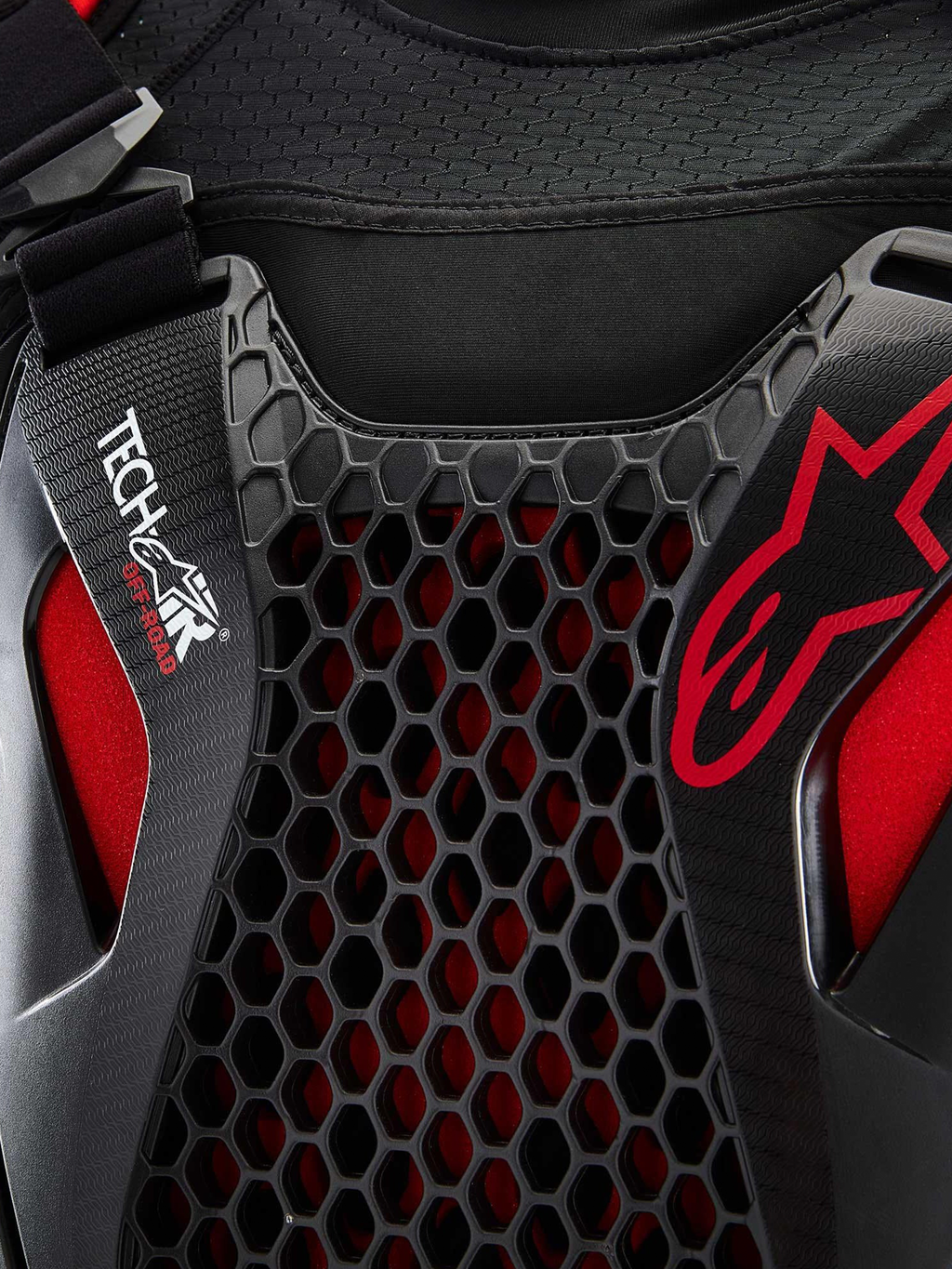 Alpinestars Airbag Tech-Air® Off-Road, pormenor em plano aproximado do sistema de airbag para motociclismo todo-o-terreno, preto e vermelho, com proteção de peito em favo de mel Nucleon CELL, logótipo Tech-Air e estrutura em malha elástica respirável
