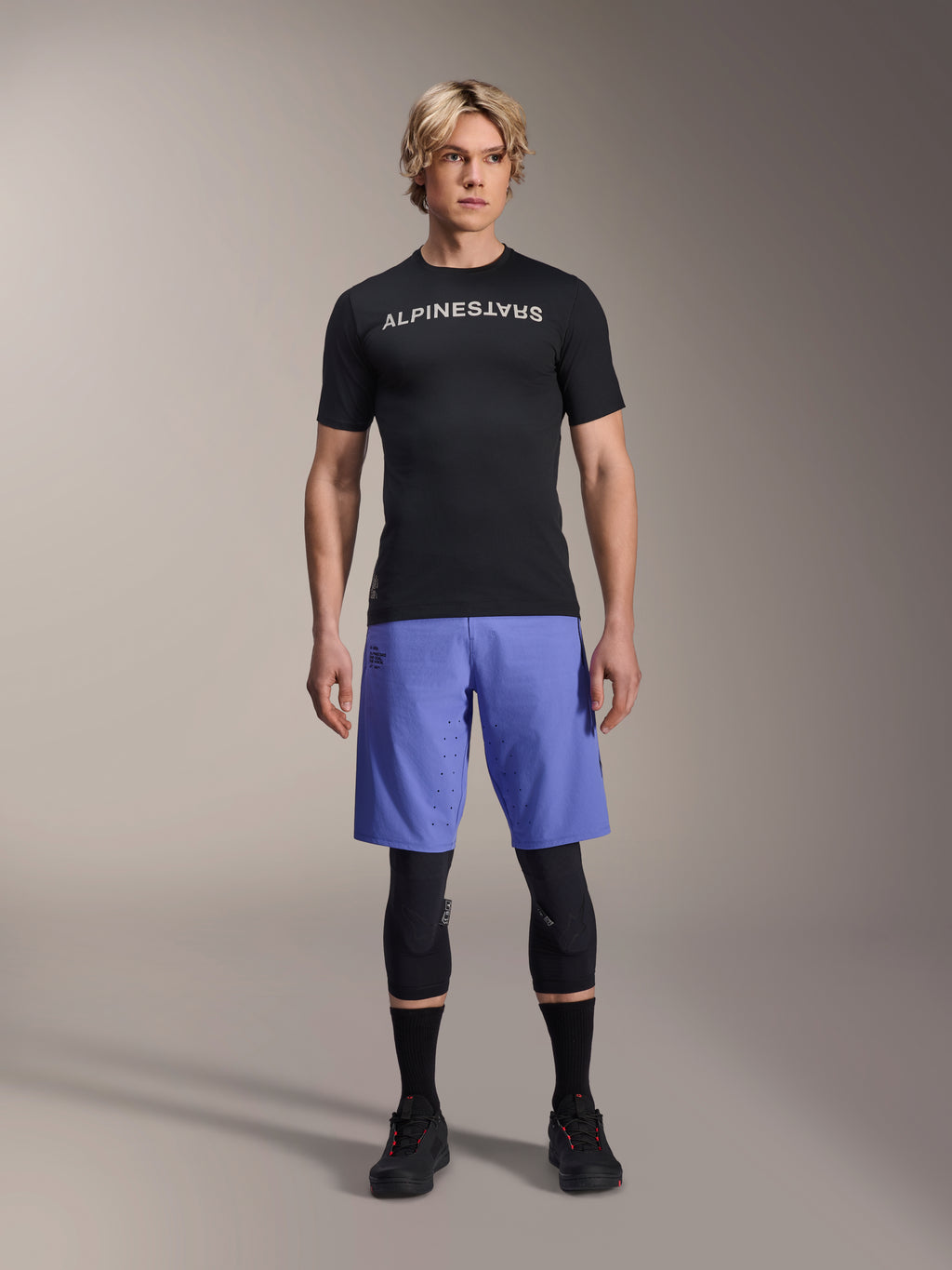 Alpinestars A-Aria Lite Short em Baja Blue, calções de BTT para homem, usados com uma camisola de manga curta preta e joelheiras de proteção, com perfurações a laser para ventilação, equipamento de performance para mountain bike