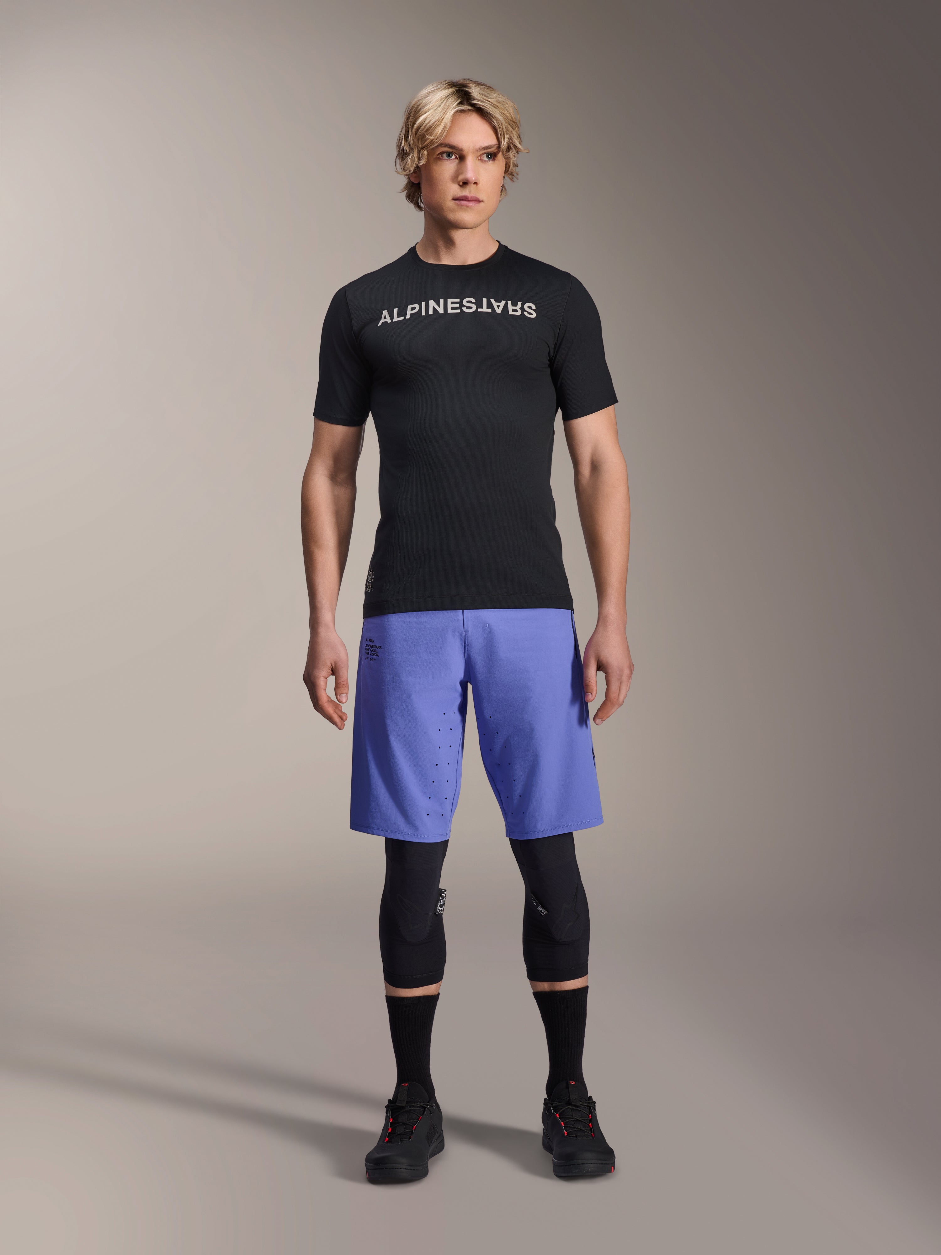 Alpinestars A-Aria Lite Short em Baja Blue, calções de BTT para homem, usados com uma camisola de manga curta preta e joelheiras de proteção, com perfurações a laser para ventilação, equipamento de performance para mountain bike