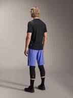 Modelo masculino visto de costas a usar calções Alpinestars A-Aria Lite em Baja Blue, combinados com uma camisola preta de manga curta e joelheiras pretas, vestuário de ciclismo MTB profissional para trilhos.