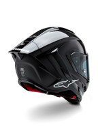 Capacete Alpinestars Supertech R10 Solid, capacete de corrida para motociclismo, acabamento em carbono preto mate e brilhante, vista traseira de três quartos mostrando o casco em fibra de carbono, spoiler aerodinâmico e logótipo Alpinestars