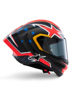 Capacete Alpinestars Supertech R10 Miller Limited Edition, capacete integral de corrida, carbono mate com gráficos vermelhos, brancos e azuis, detalhes de estrelas azuis e acabamento da viseira em amarelo, perfil aerodinâmico com viseira fumada escura, equipamento de segurança de motociclismo de alta performance