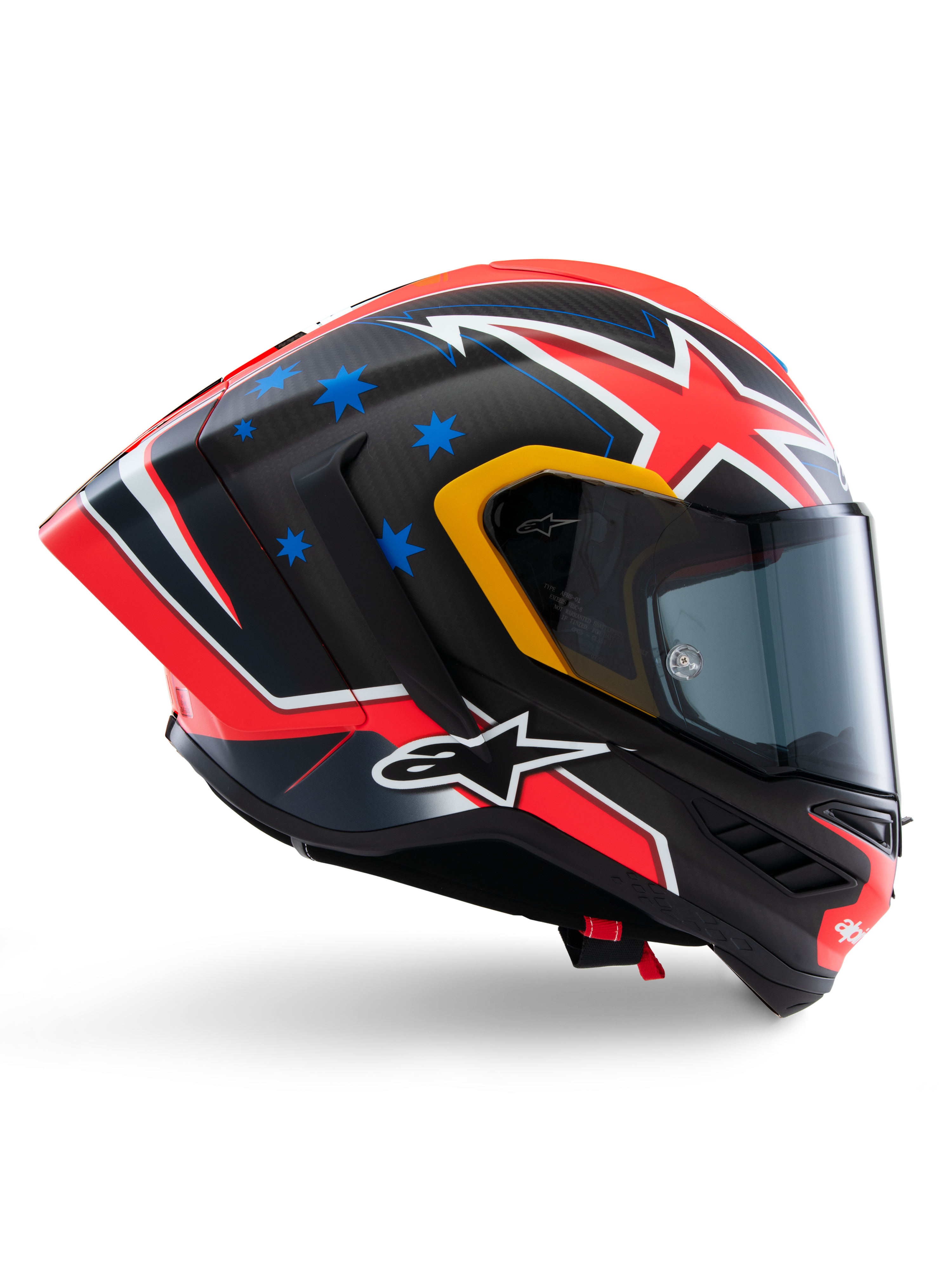 Capacete Alpinestars Supertech R10 Miller Limited Edition, capacete integral de corrida, carbono mate com gráficos vermelhos, brancos e azuis, detalhes de estrelas azuis e acabamento da viseira em amarelo, perfil aerodinâmico com viseira fumada escura, equipamento de segurança de motociclismo de alta performance