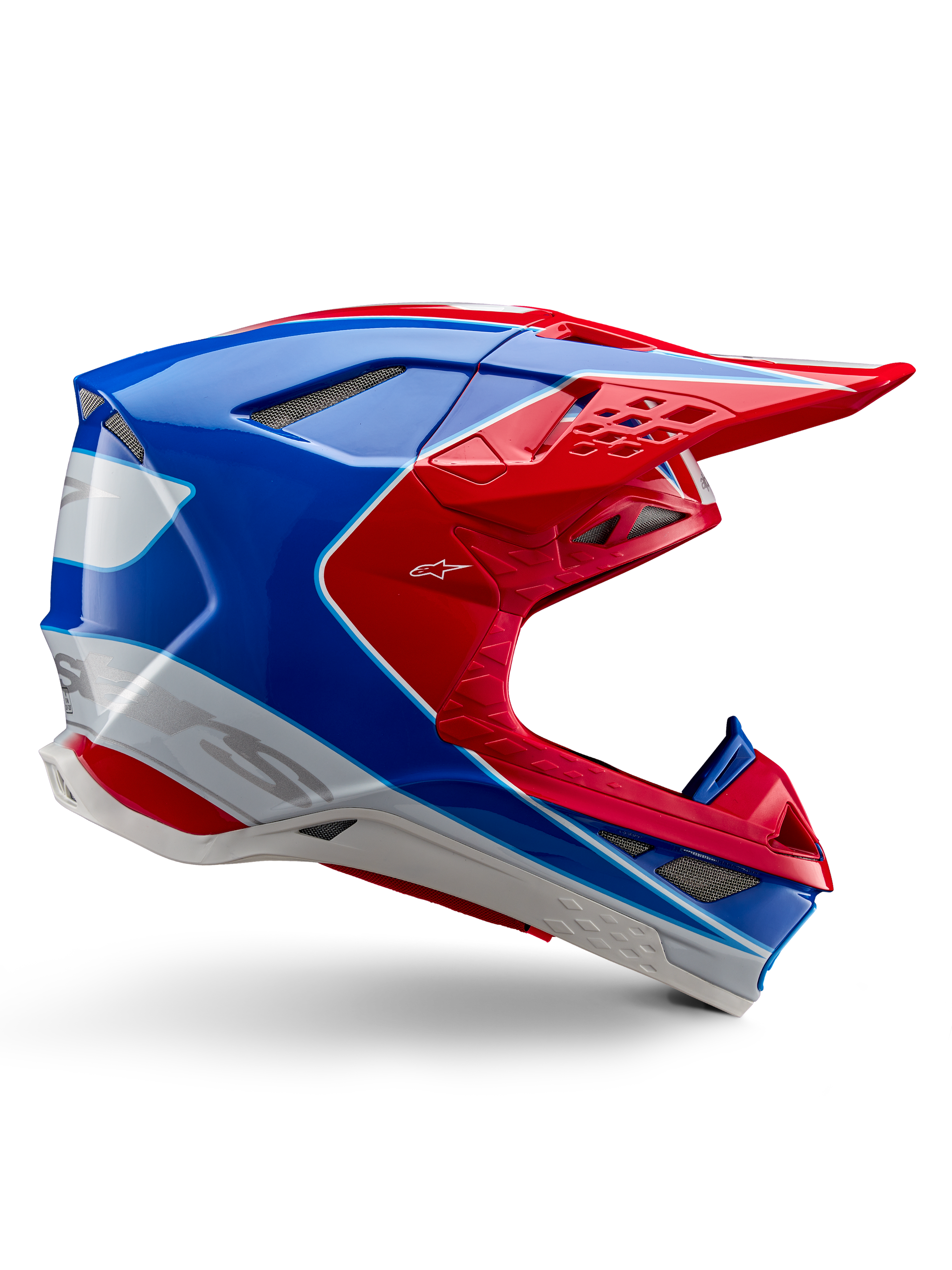 Capacete Alpinestars Supertech M10 Aeon, capacete de corrida de motocross, vermelho vivo, azul e branco, acabamento brilhante, perfil lateral aerodinâmico com múltiplas aberturas de ventilação cobertas por malha, contornos angulares e pala
