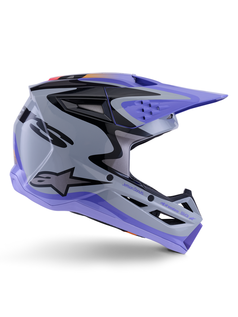 Alpinestars S-M3 Jettson Helmet ECE 22.06, capacete de motocross, cinzento, roxo e preto brilhante, vista de perfil com viseira e queixeira roxas, calota aerodinâmica elegante com gráficos pretos, múltiplas aberturas de ventilação e marca "Jettson Donuts" na lateral.