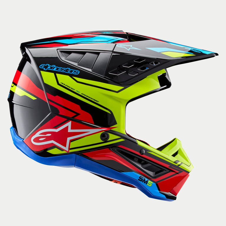 Alpinestars S-M5 Action 2 Helmet ECE, capacete de motocross, preto brilhante com grafismos em amarelo fluorescente, vermelho vivo e azul ciano, vista de perfil com calota aerodinâmica, pala ventilada e marca Alpinestars em destaque na lateral, proteção profissional para corridas todo-o-terreno