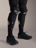 Joelheiras Alpinestars A-Impact Plasma Pro, pretas e brancas, com a marca da tecnologia Nucleon PLASMA, usadas com meias pretas e sapatos de BTT pretos, tiras de ajuste seguras, equipamento de proteção ergonómico para ciclismo todo-o-terreno