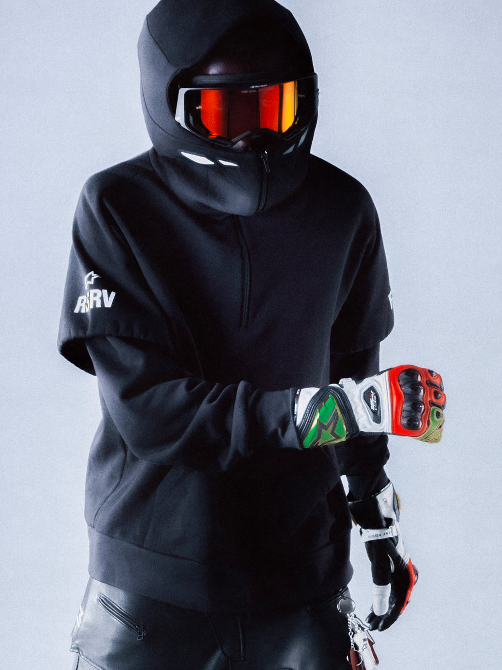 Alpinestars RSRV Vault Hoodie, sweatshirt preta com capuz para estilo urbano, pessoa com capacete e luvas coloridas, logótipos brancos na manga, visual futurista de proteção