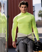 Alpinestars ZX Evo V3 Top - Manga Comprida, camada de base para automobilismo, amarelo fluo, usado por um piloto com um fato de condução cinzento atado à cintura, a segurar um capacete preto, apresentando o logótipo Alpinestars no pescoço e nos ombros, equipamento técnico que afasta a humidade para desportos motorizados