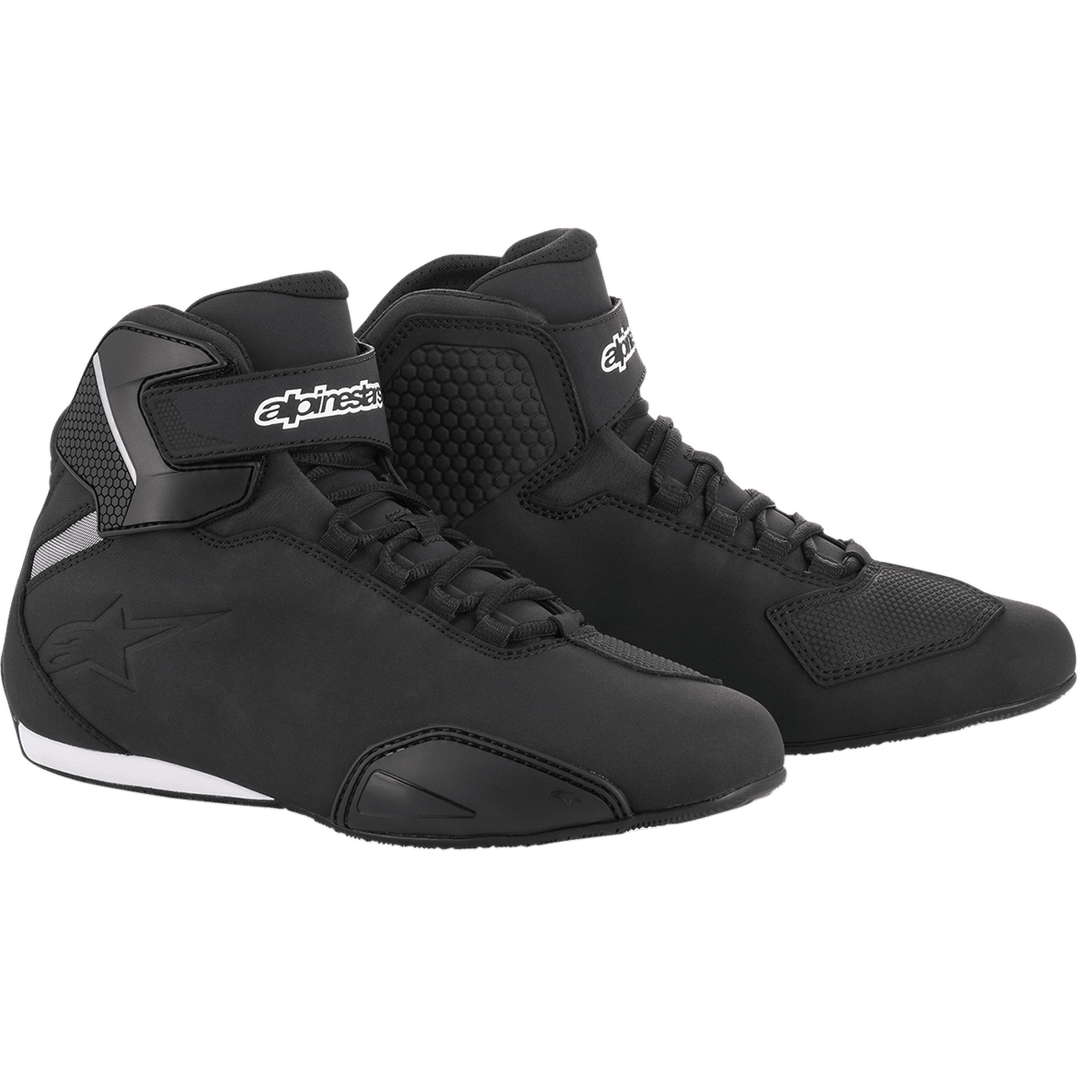 These black high-top Sektor Shoes by Alpinestars EU showcase a modern design, featuring a black textured pattern on the sides, a logo on the ankle straps, and white accents on the back and sole. They boast a speed lacing system and durable microfiber construction for a sleek, sporty appearance.