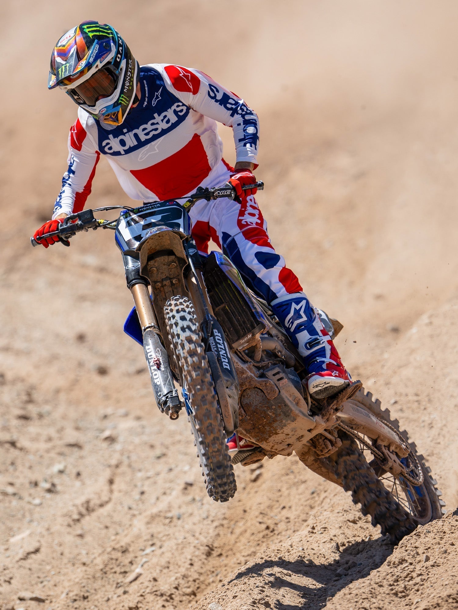 Motocross rider in action on a dirt track, wearing the Limited Edition Techstar Fortitude Jersey in Bright Red White and Blue, coordinated with matching racing pants and boots, featuring bold Alpinestars branding, professional off-road racing apparel